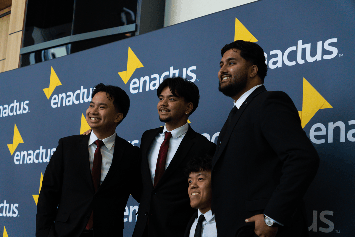 People posing for a photo in front of a wall with the Enactus logo.